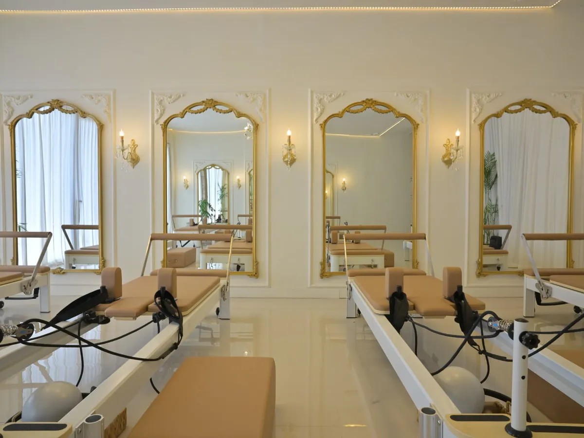 A row of caramel reformers facing gold framed mirrors and wall sconces